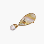 Iridescent shell brooch with gold bird accent and wire-wrapped baroque pearl drop on cream background.